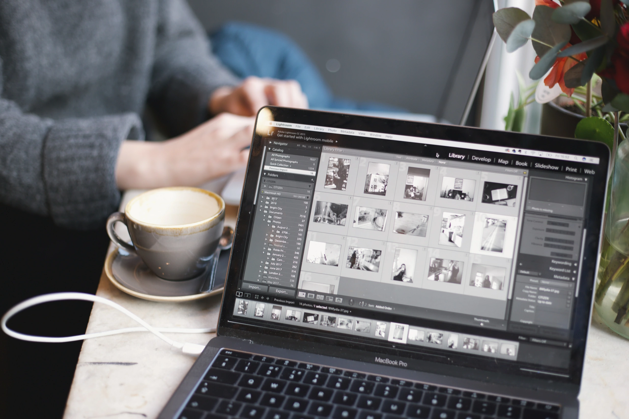 Un ordinateur portable équipé du logiciel de retouche photo Lightroom affiche des vignettes d'images en noir et blanc ; une station de travail est visible à l'arrière-plan.