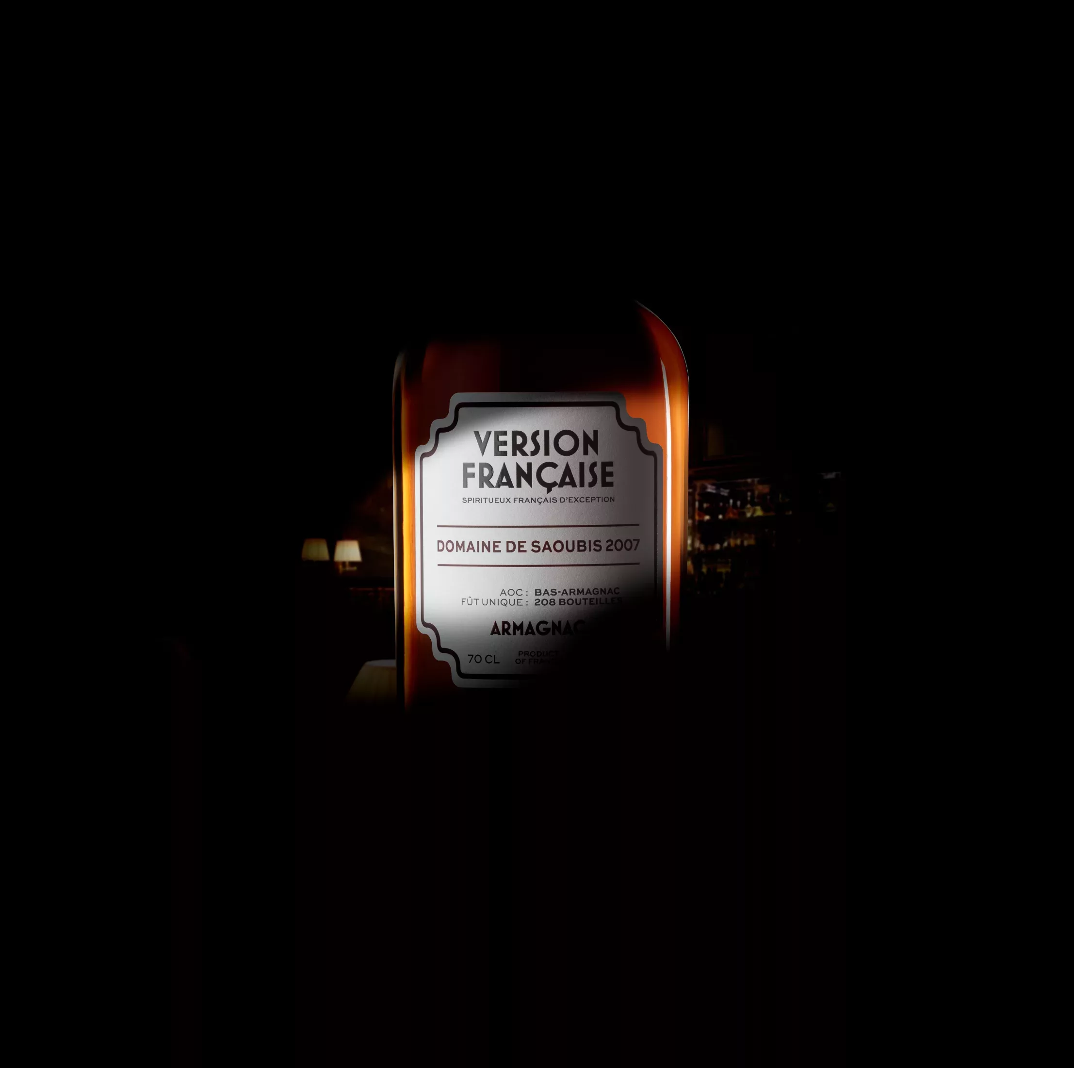 Une bouteille d'armagnac étiquetée Version Française Domaine de Saoubis 2007 est centrée et éclairée sur un fond sombre, la mise au point est nette.