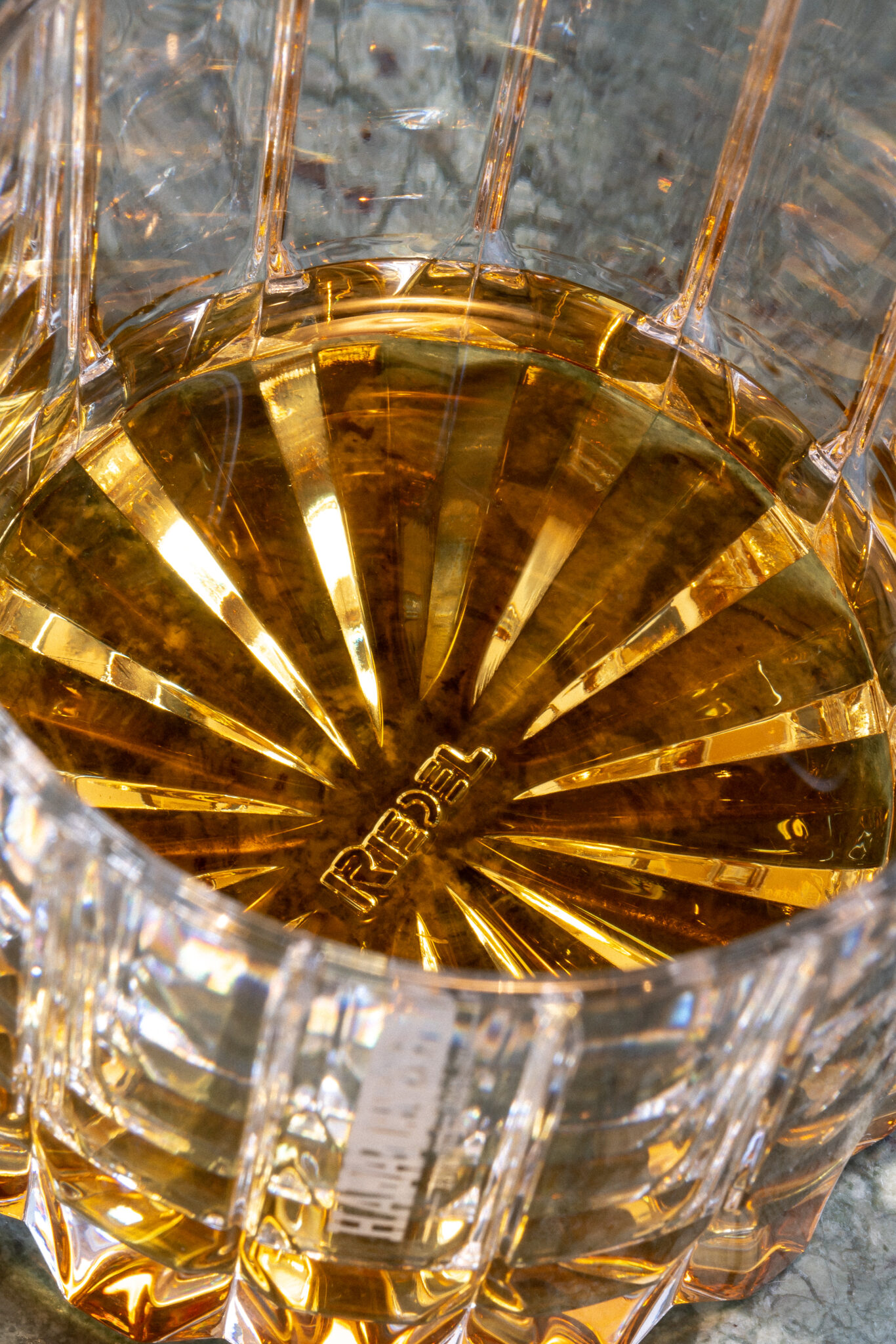 Packshot Hampden Verre Gros plan d'un verre à facettes contenant un liquide ambré, probablement du whisky, sur une surface texturée grise ; la base porte l'inscription "REBEL".