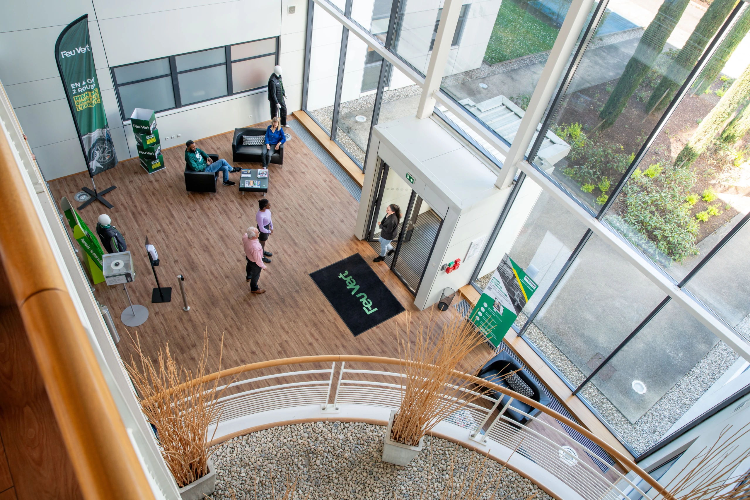 Perspective aérienne d'un hall d'entrée d'entreprise avec de grandes fenêtres, des occupants sur des canapés, une entrée en verre et des bannières portant le logo RevWorx ; photographie d'entreprise.