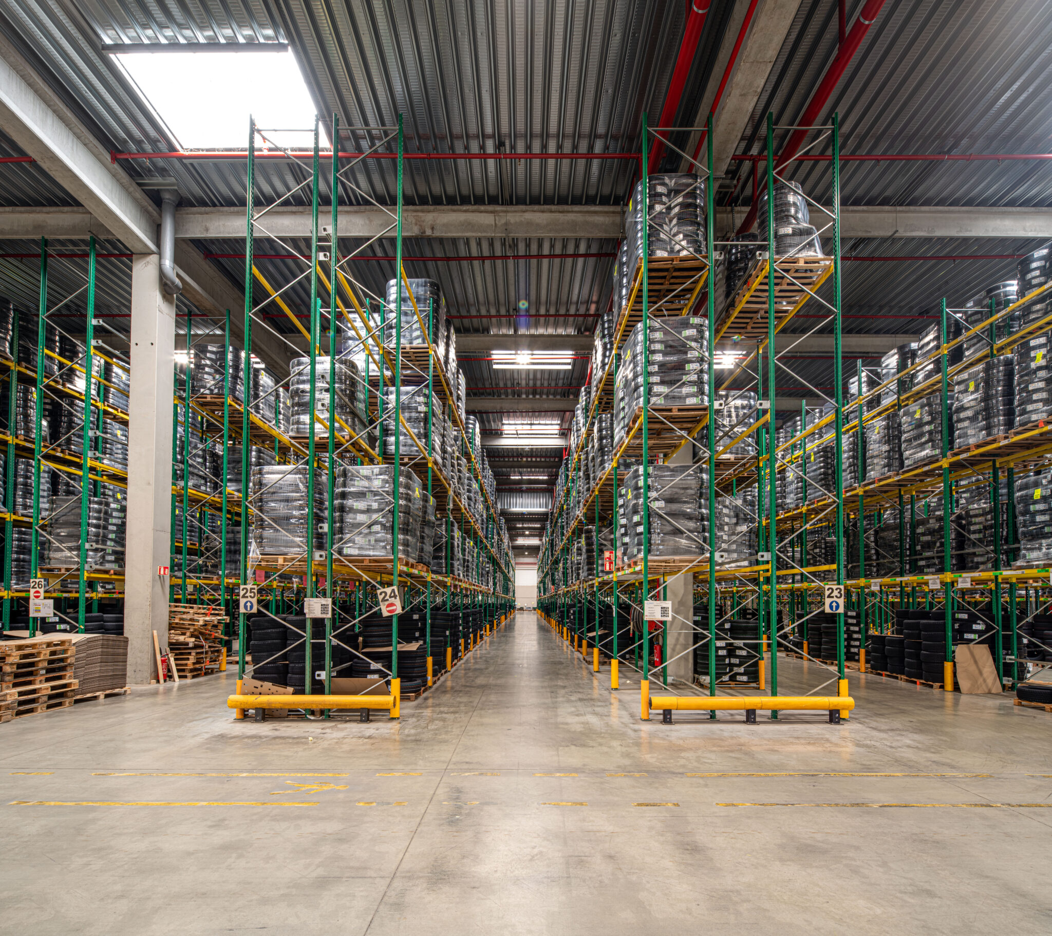 Reportage Photo Corporate Logistique Feu Vert 4 Intérieur d'un entrepôt dans le Rhône avec de hauts rayonnages métalliques, des marchandises palettisées et une large allée éclairée par des plafonniers industriels, reportage.