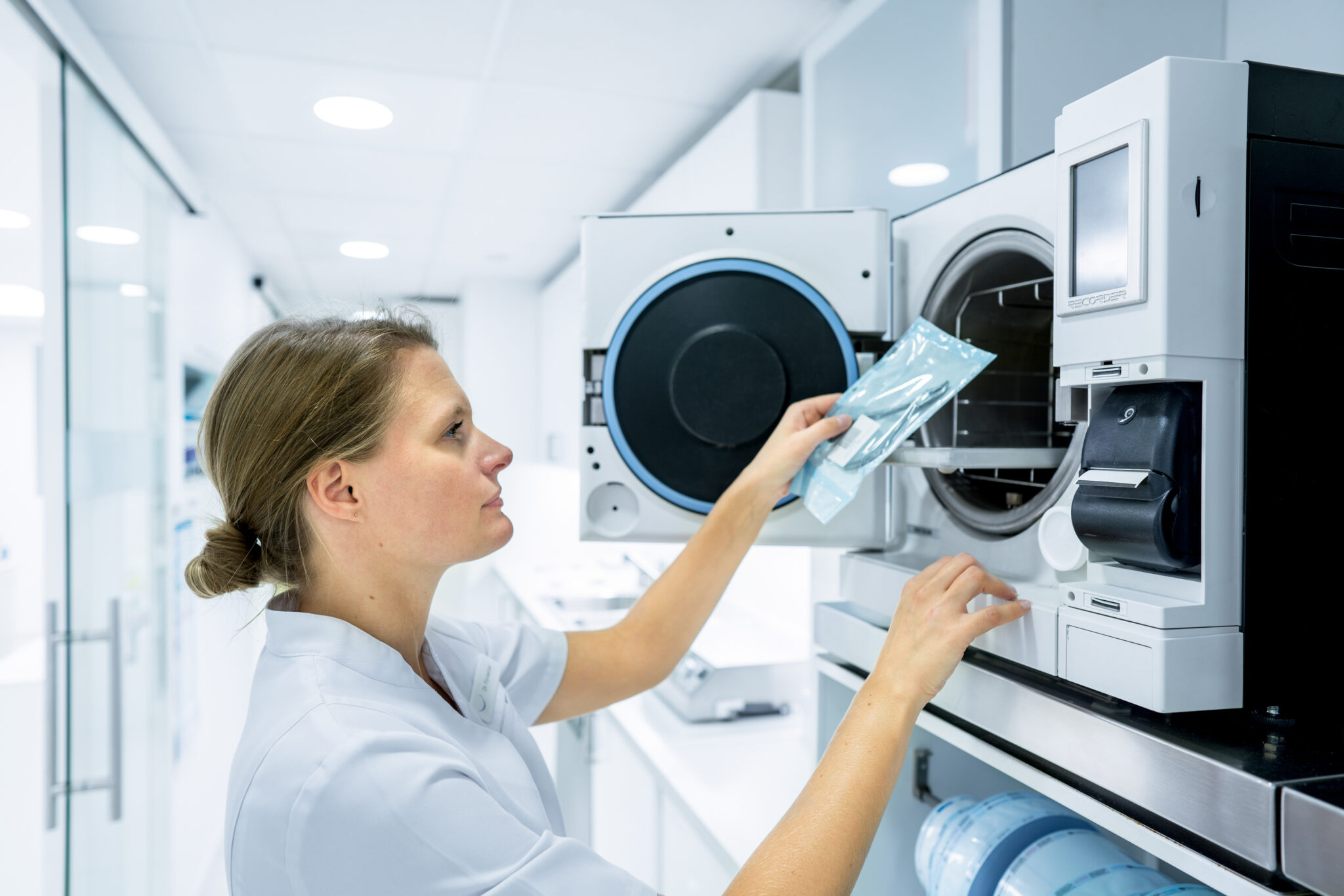 shooting Apident mise en scène 2 Une femme en blouse blanche charge un emballage scellé dans une machine de stérilisation dans une clinique bien éclairée lors d'une séance photo avec un orthodontiste.