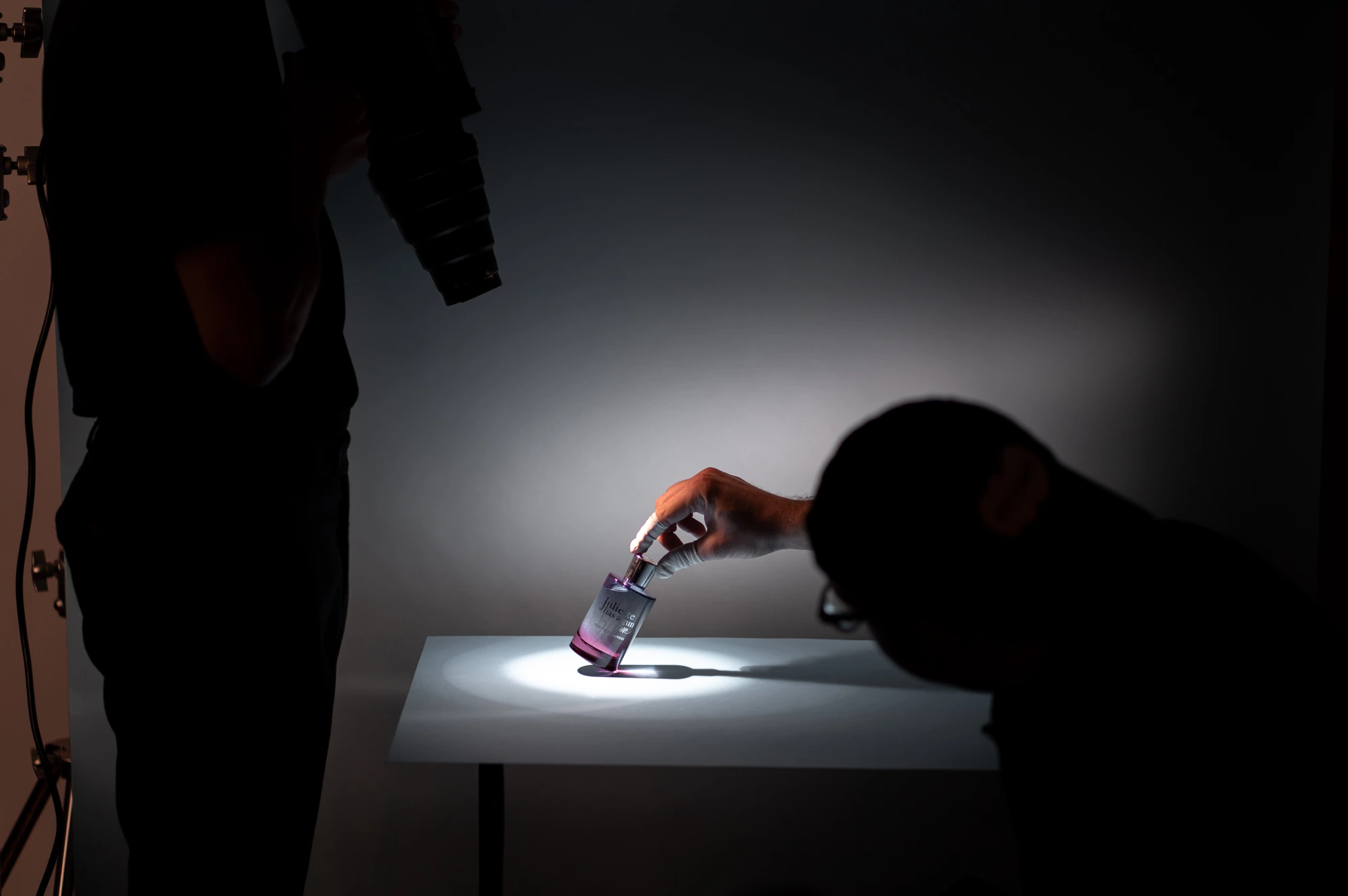 Dans un studio contrôlé, un photographe capture un sujet tenant un bécher sous un éclairage ciblé sur une surface blanche.