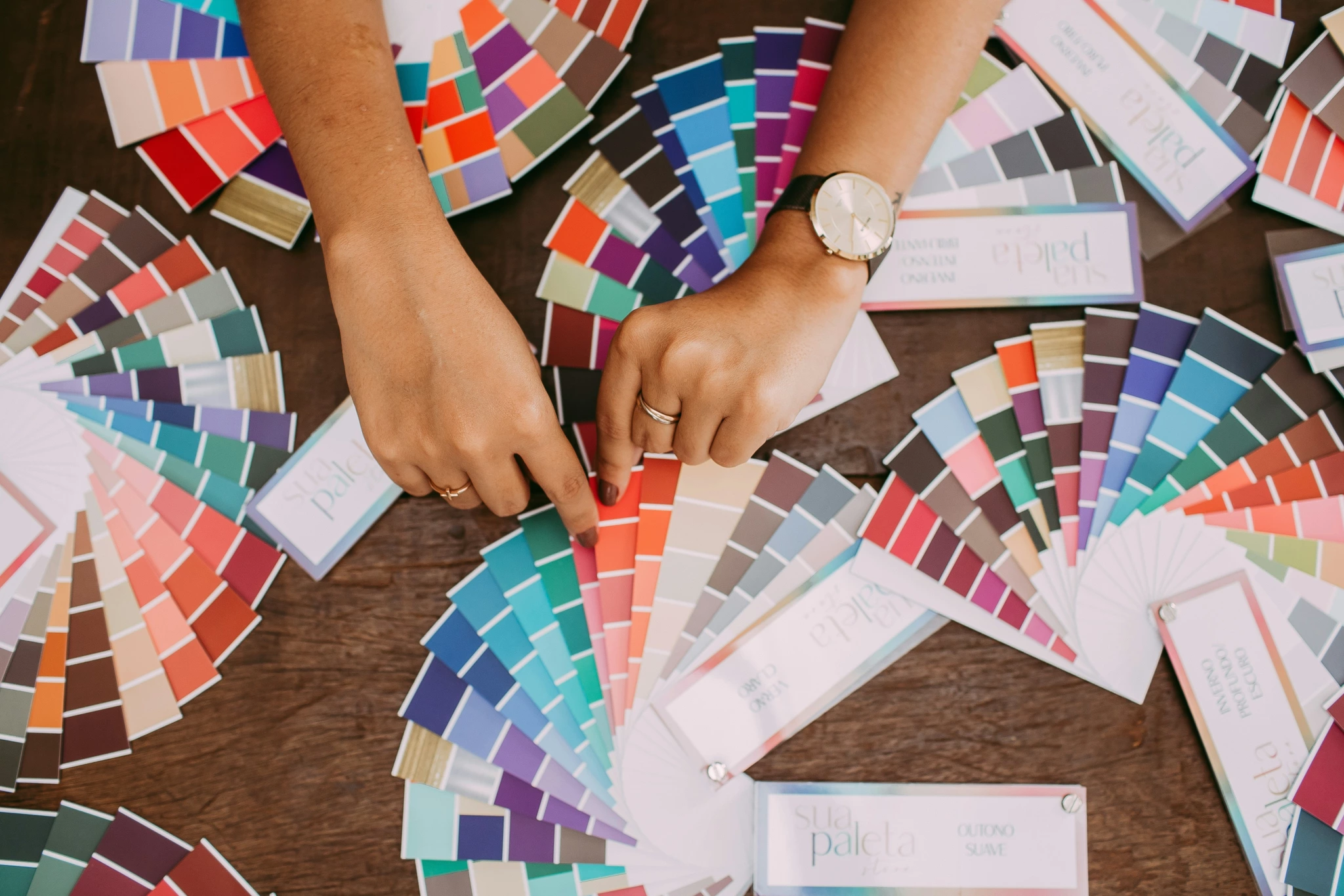 Une main gauche portant une montre et des bagues montre des échantillons de couleurs de peinture sur une table, adaptée à un studio de photographie de produits.