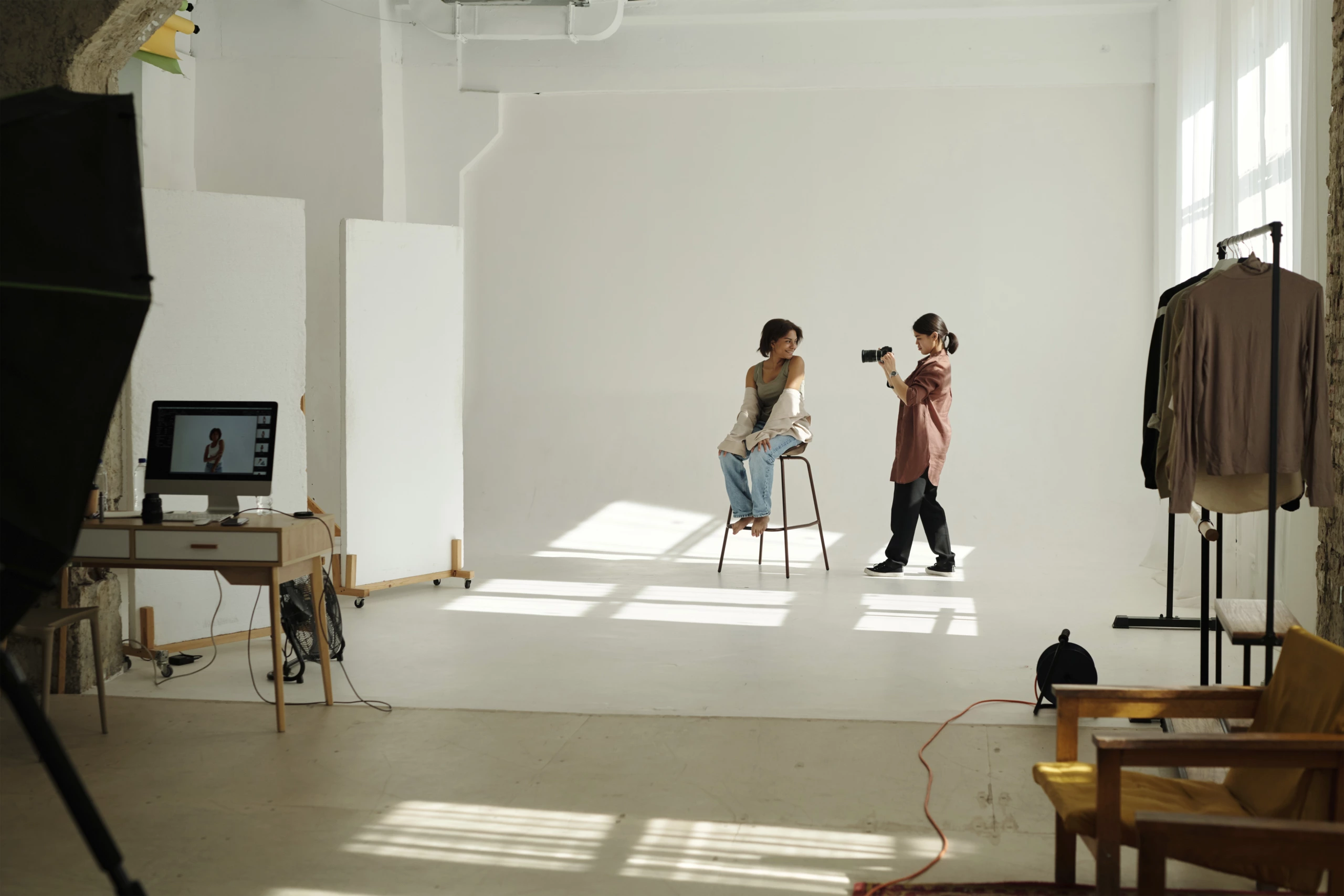 Le photographe capture un sujet assis dans un studio bien éclairé avec du matériel d'éclairage, des portants de vêtements et un moniteur à l'arrière-plan.