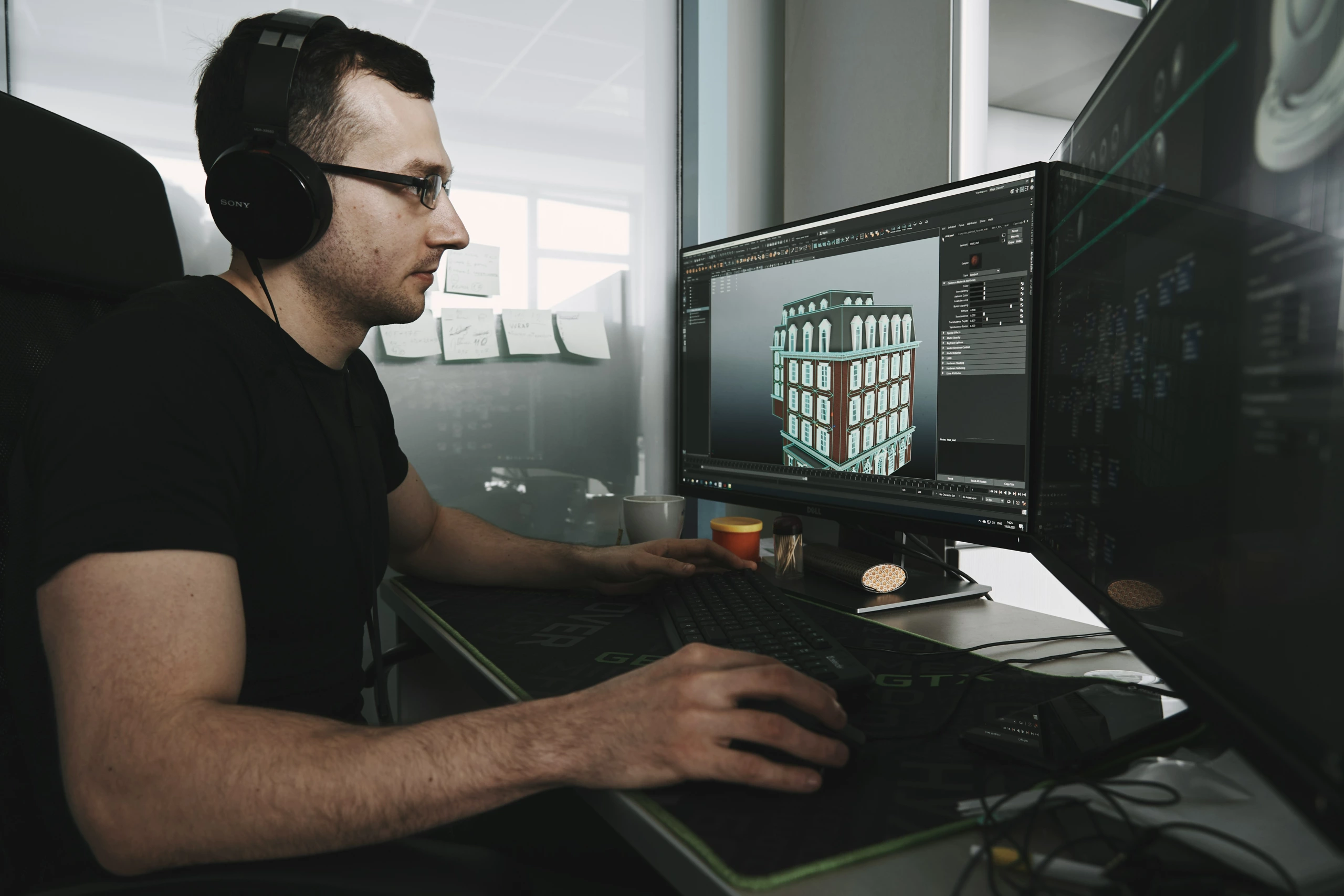 Un technicien de studio portant des écouteurs effectue le montage sur deux moniteurs, l'un avec un logiciel de modélisation 3D et l'autre avec une interface de codage.