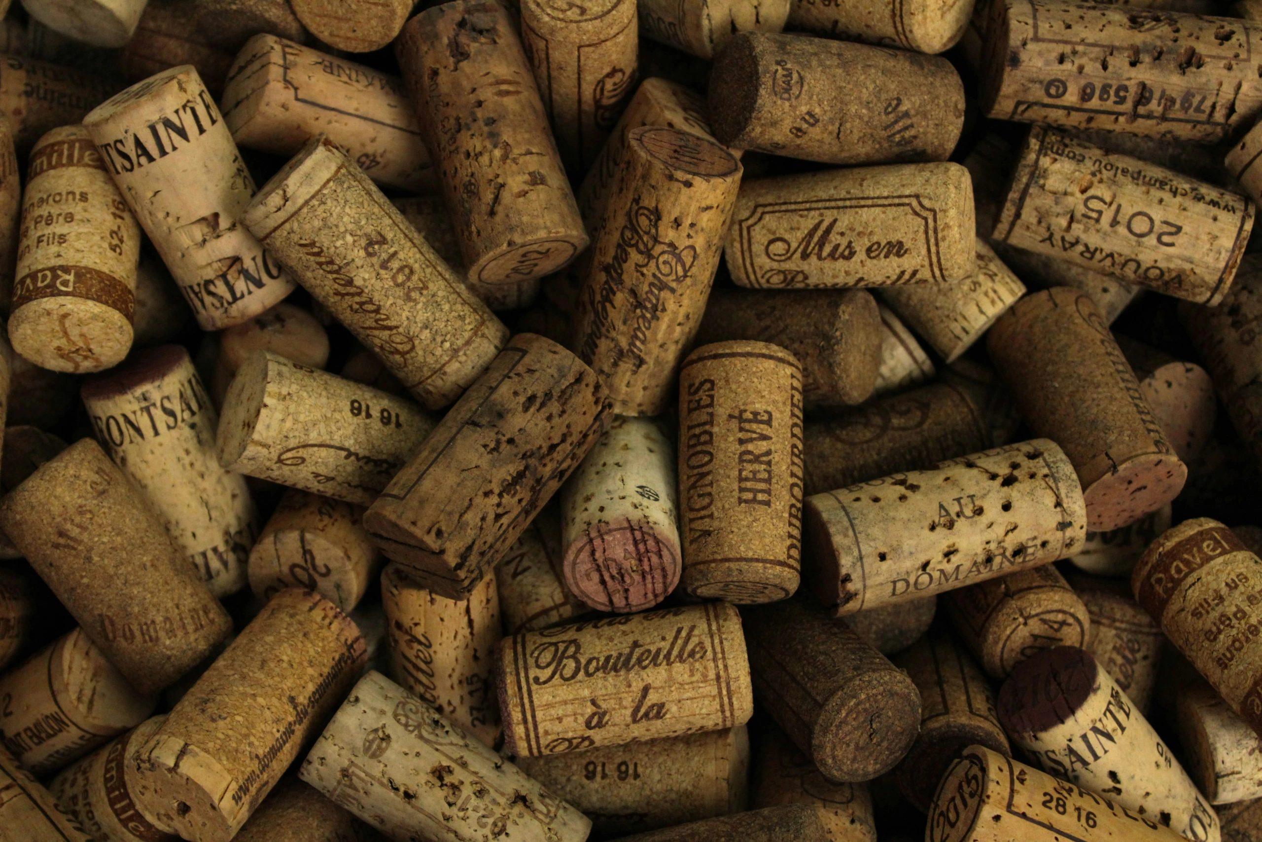 Photographie en gros plan d'un assortiment de bouchons de vin usagés présentant diverses empreintes, marques et couleurs avec des signes visibles d'âge et de taches.