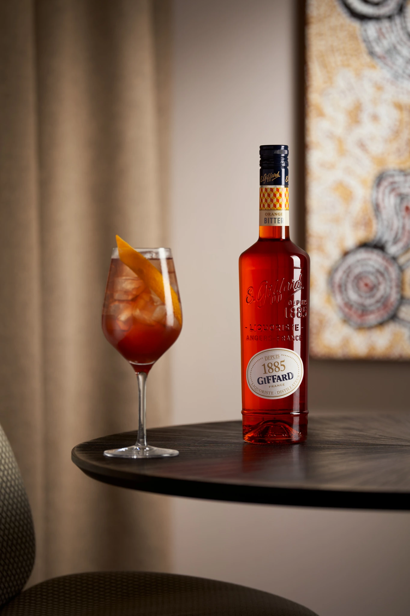 Giffard Orange Bitter Bouteille d'apéritif Giffard Anisé et verre à vin avec cocktail rougeâtre et écorce d'orange sur une table sombre ; fond d'art flou ; éclairage de studio.
