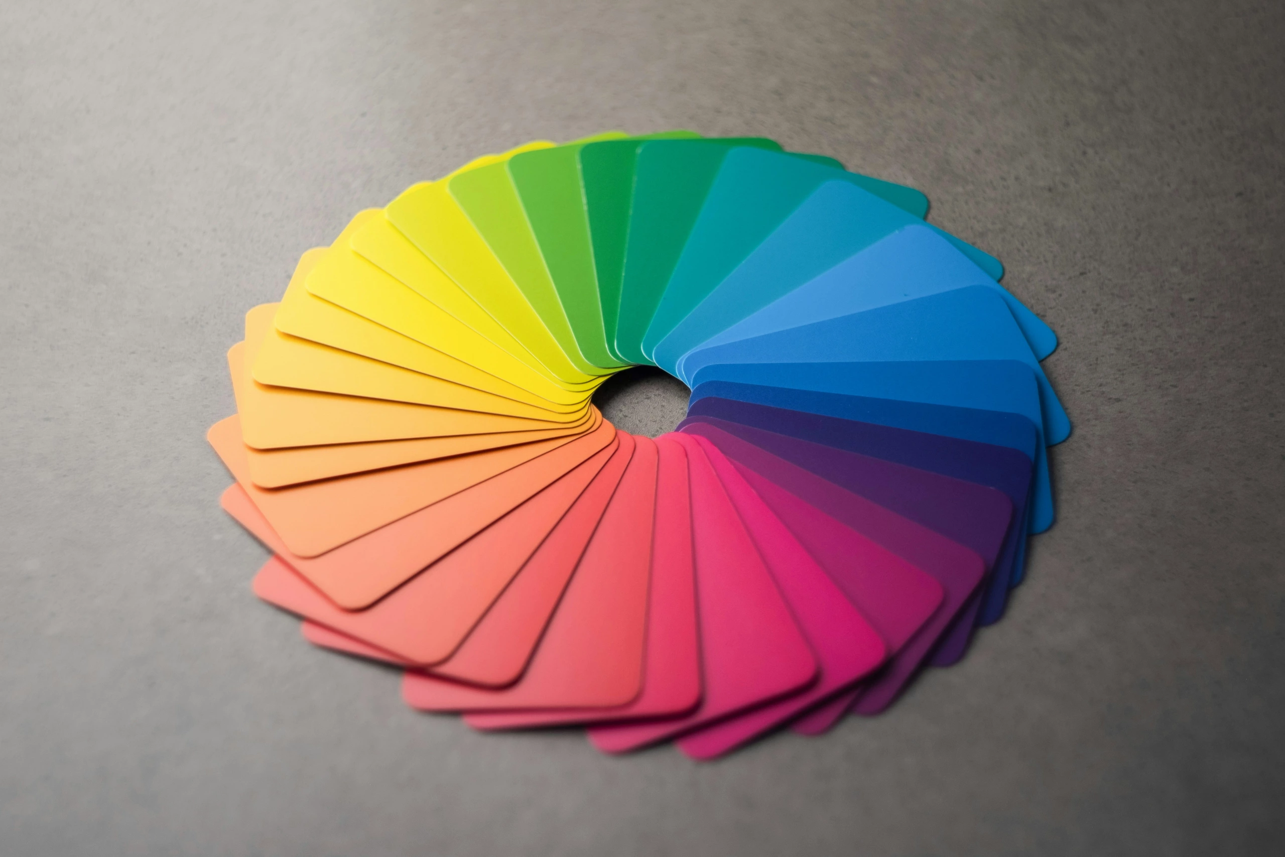 Des échantillons de couleur rectangulaires disposés en cercle passent du rouge au violet, ressemblant à une impression en photogravure sur un fond gris.