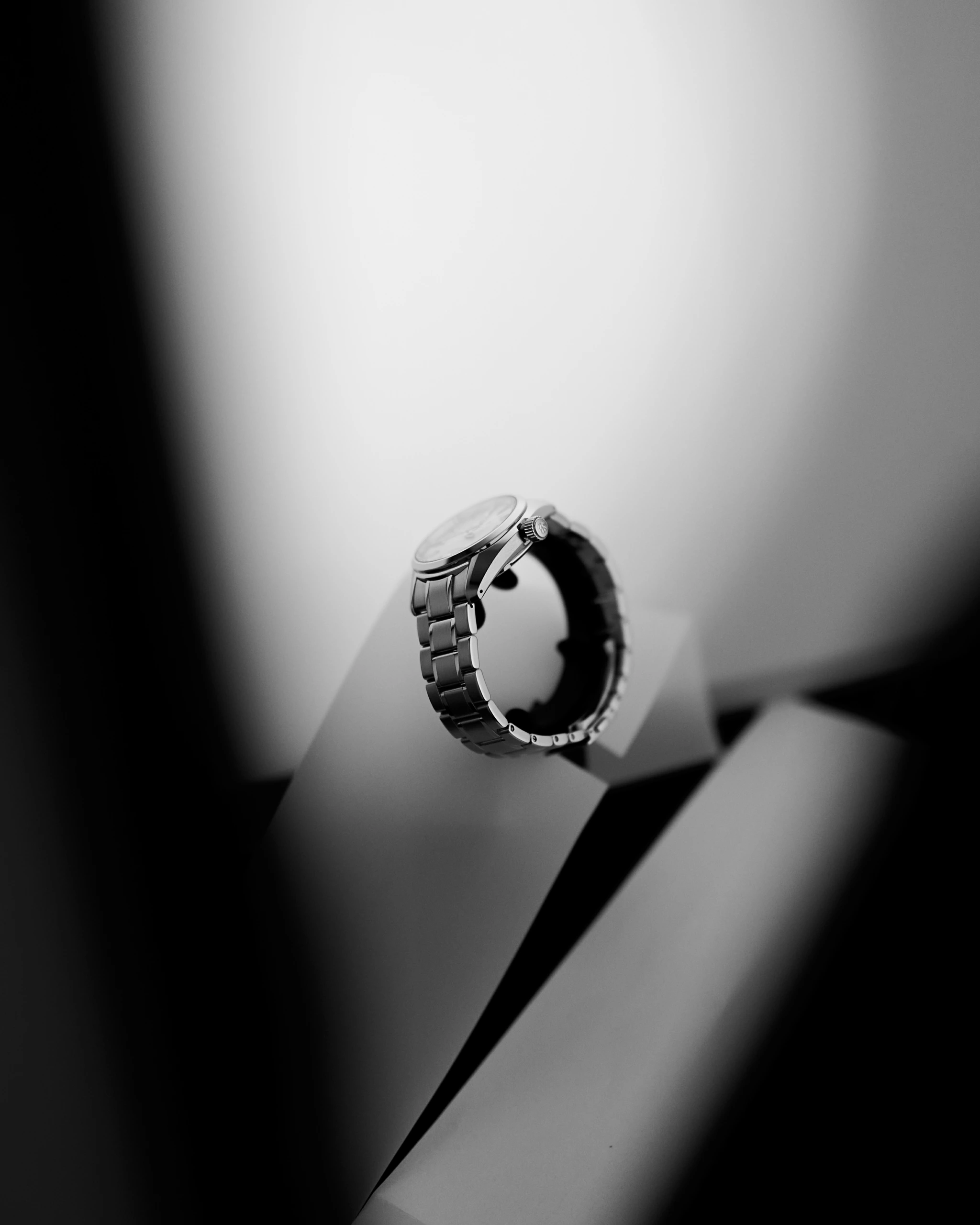 Une montre-bracelet en argent se tient debout sur des surfaces géométriques dans une prise de vue en studio en noir et blanc, mettant en évidence des techniques de retouche subtiles.