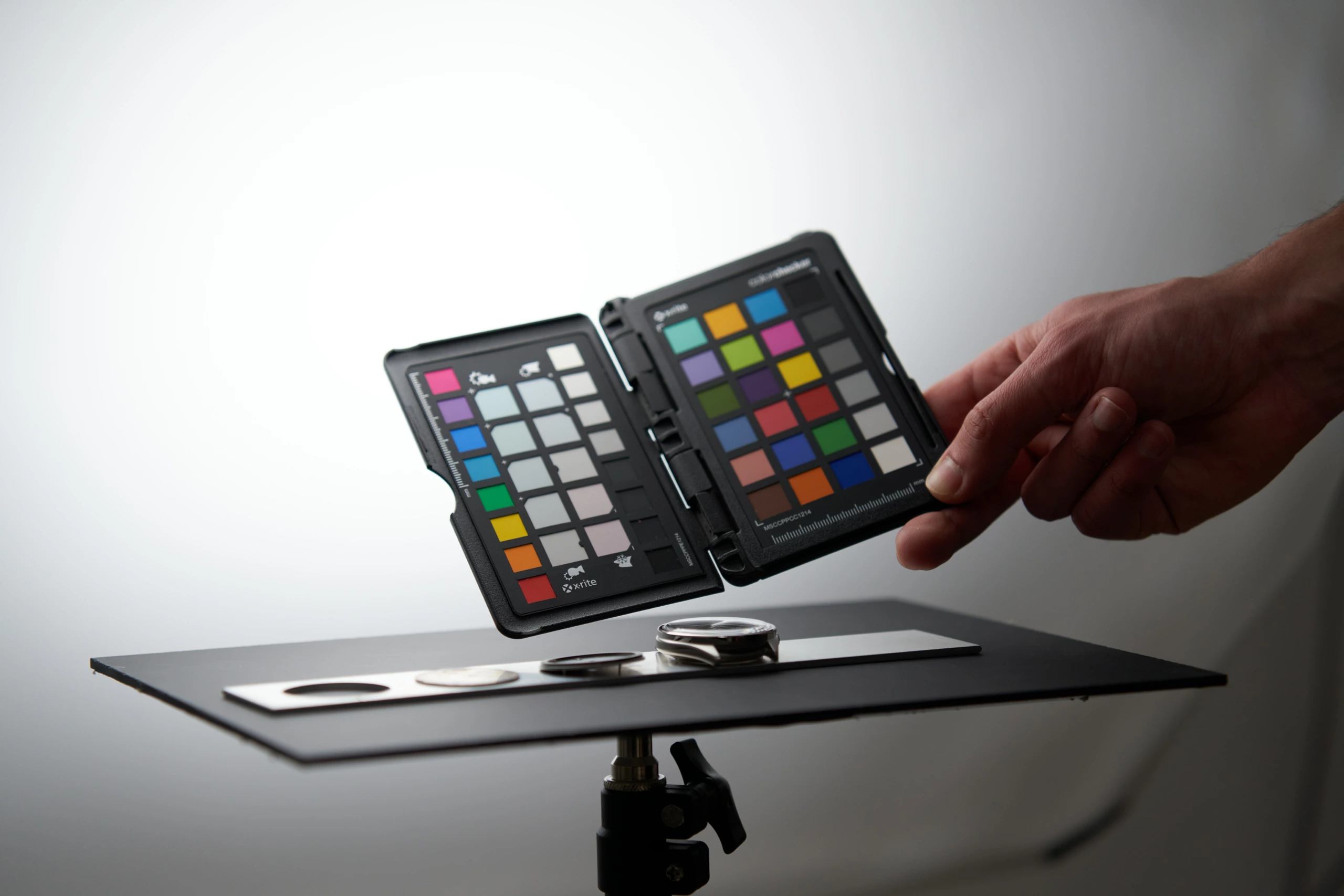 Main tenant une charte colorimétrique au-dessus d’une montre posée sur une table de studio