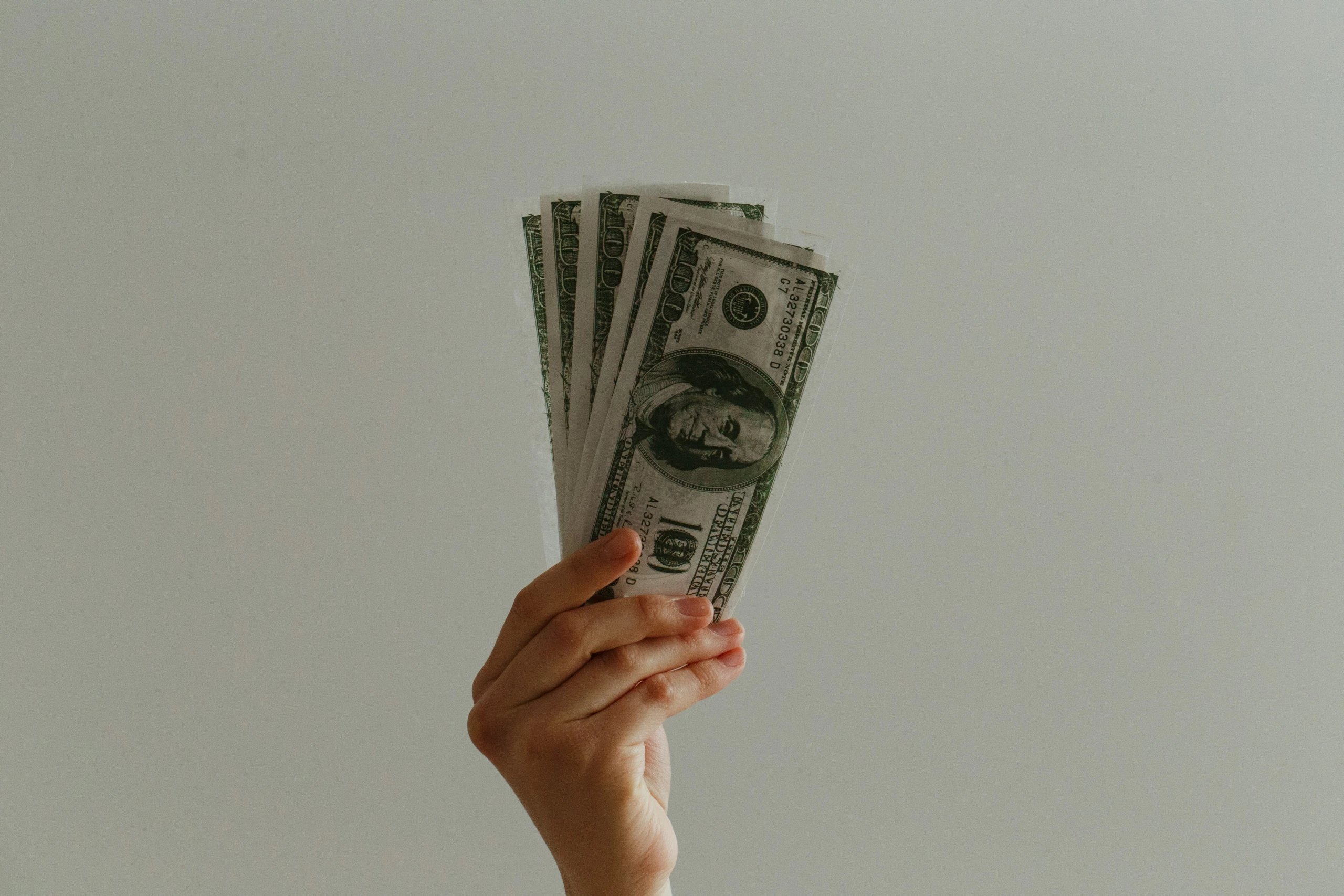 Une main présente quatre billets de 100 dollars américains sur un fond neutre, représentant visuellement le salaire d'un retoucheur photo dans l'industrie de la photographie.