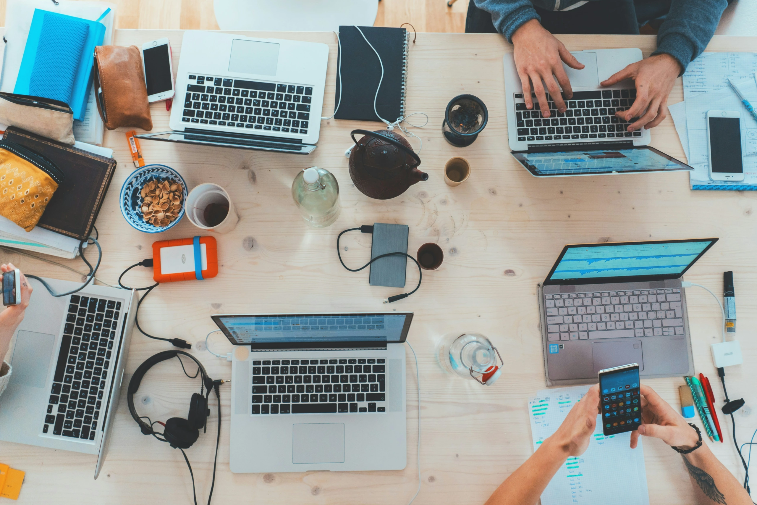 Quatre personnes collaborent autour d'une table en bois avec des ordinateurs portables, des cahiers et du matériel de bureau, idéal pour un flux de travail de retouche d'images.