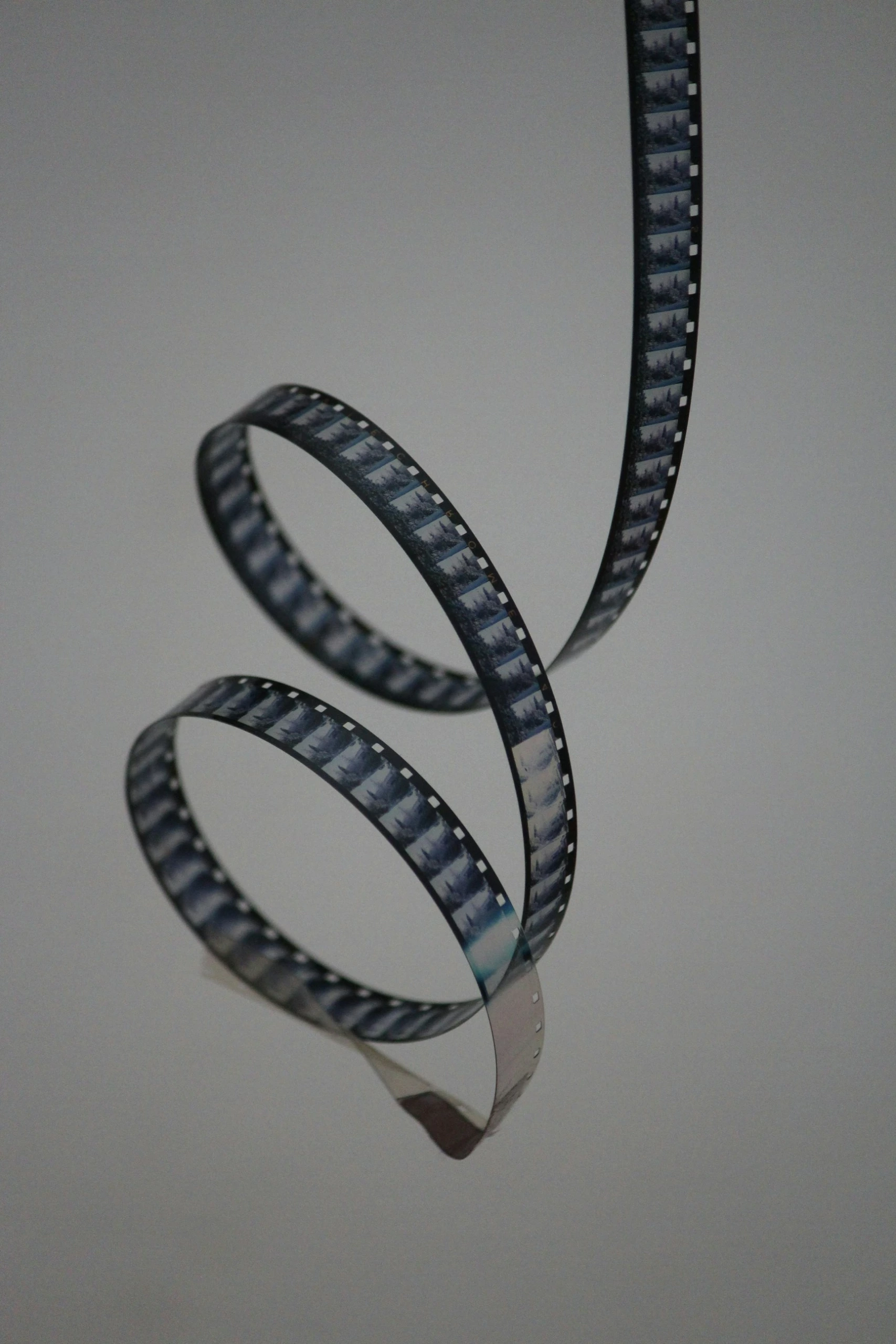 Une bande de film photographique est suspendue en spirale sur un fond lisse gris clair, faisant référence aux techniques de retouche photographique analogique.