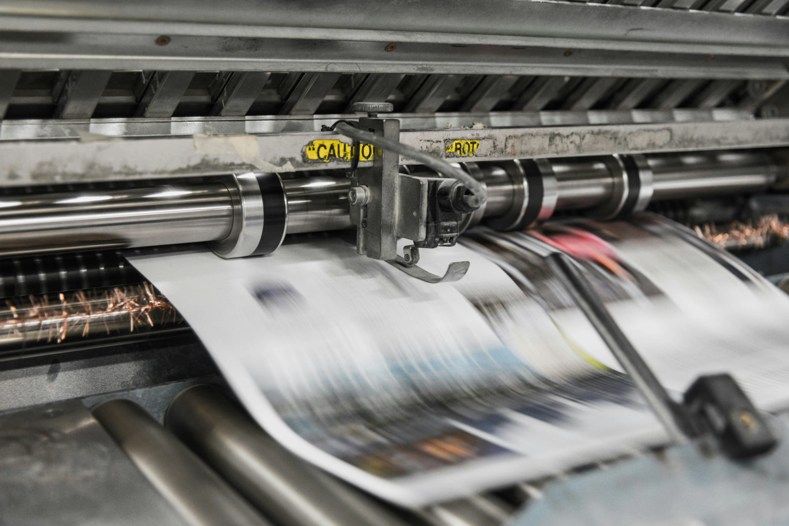 Gros plan d'une presse à imprimer à grande vitesse fonctionnant pendant le processus BAT Numérique, montrant le flou de mouvement et le mouvement du papier pour la documentation du flux de travail.
