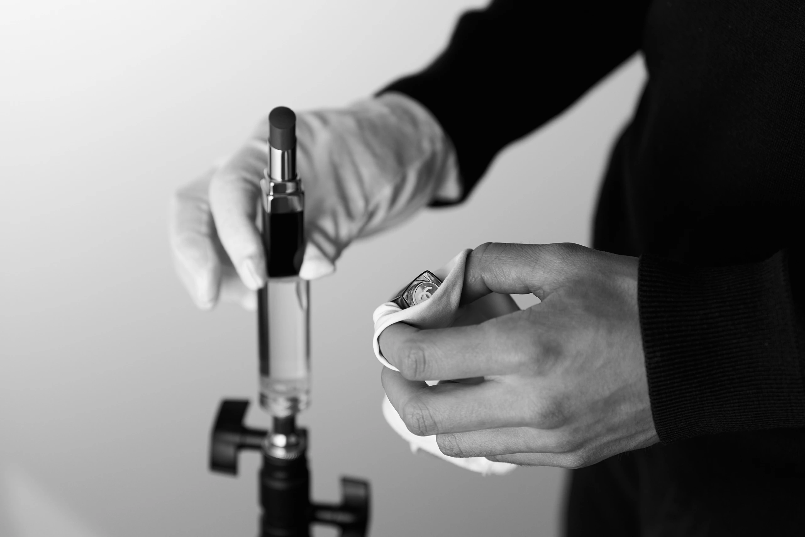 Main ajustant un rouge à lèvres noir et argenté sur un support de studio photo.