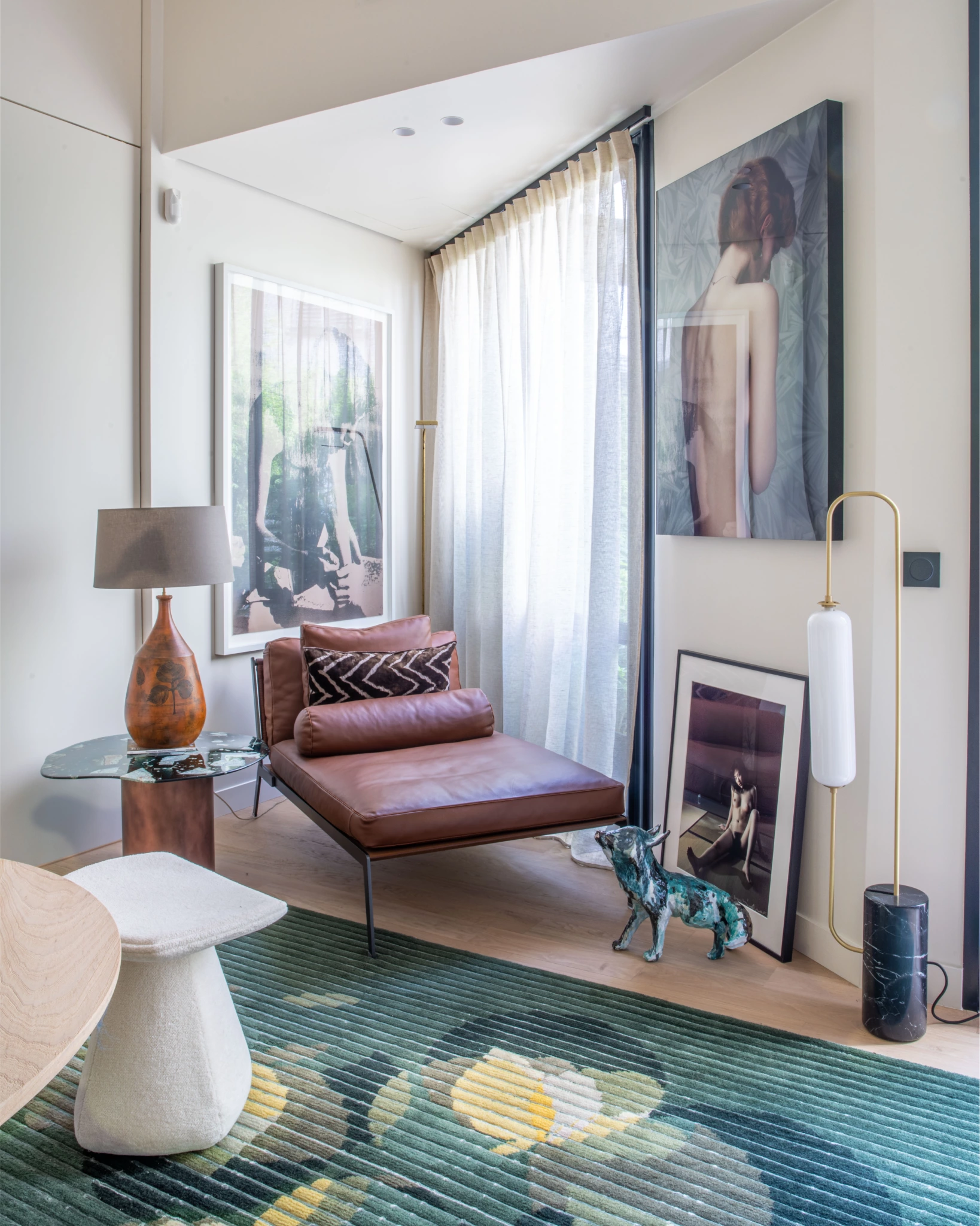 Espace de travail Paris 6ème 11 Scène d'intérieur moderne avec une chaise longue en cuir brun, une table d'appoint et une lampe en verre, un tableau encadré, un chien en céramique bleue, un tapis floral vert.