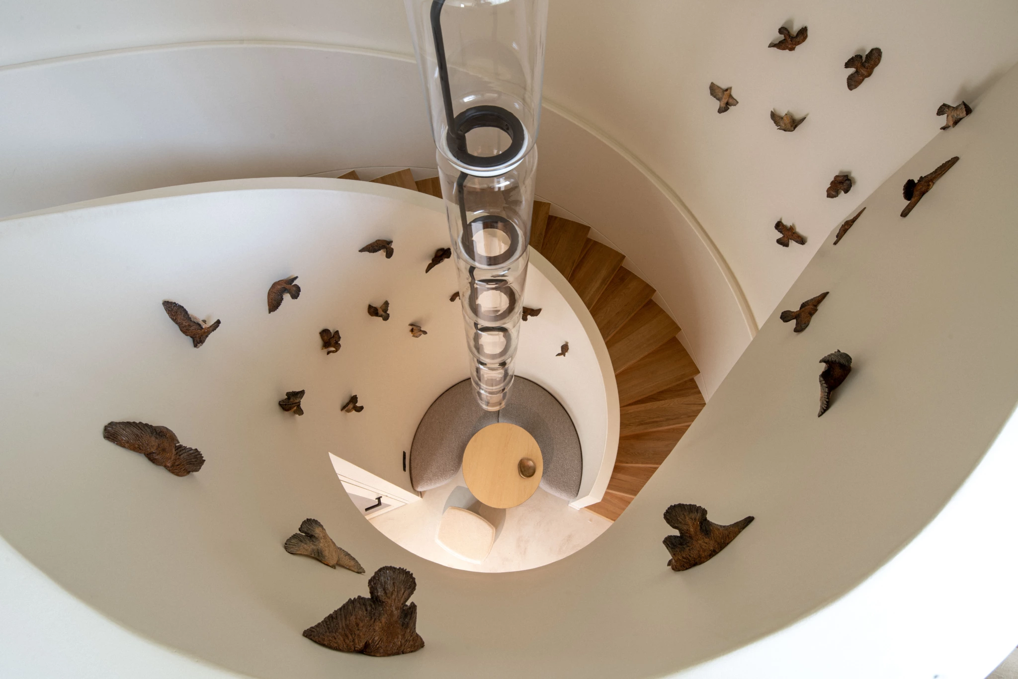 Espace de travail Paris 6ème 3 Perspective aérienne d'un escalier en colimaçon avec des marches en bois, des murs blancs sculptés avec des figures d'oiseaux, et une table ronde et une chaise en dessous.