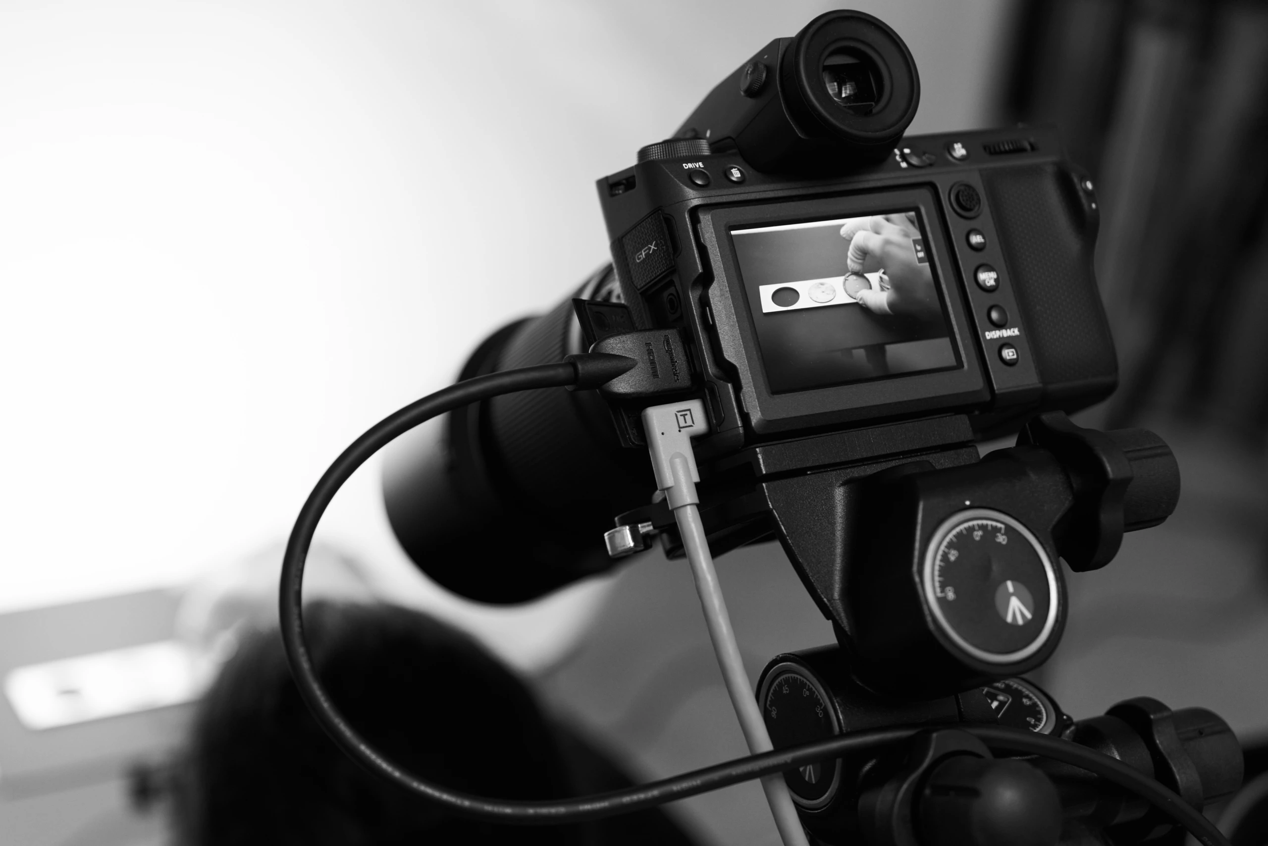 Un appareil photo monté sur trépied prend une photo macro d'une main tenant un objet ; vue en direct sur l'écran. Photographie de produit en noir et blanc.