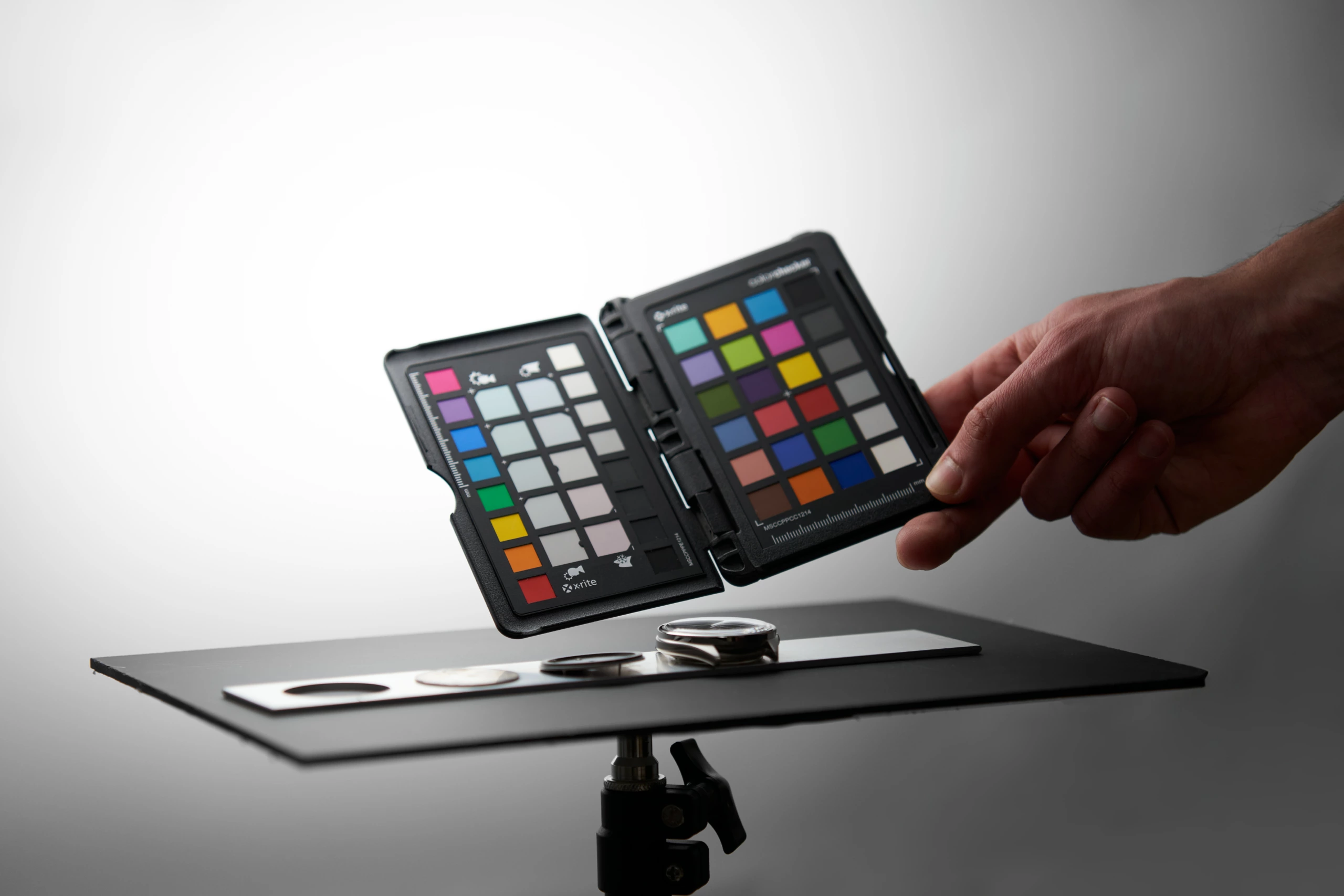Main tenant une charte colorimétrique au-dessus d’une montre posée sur une table de studio