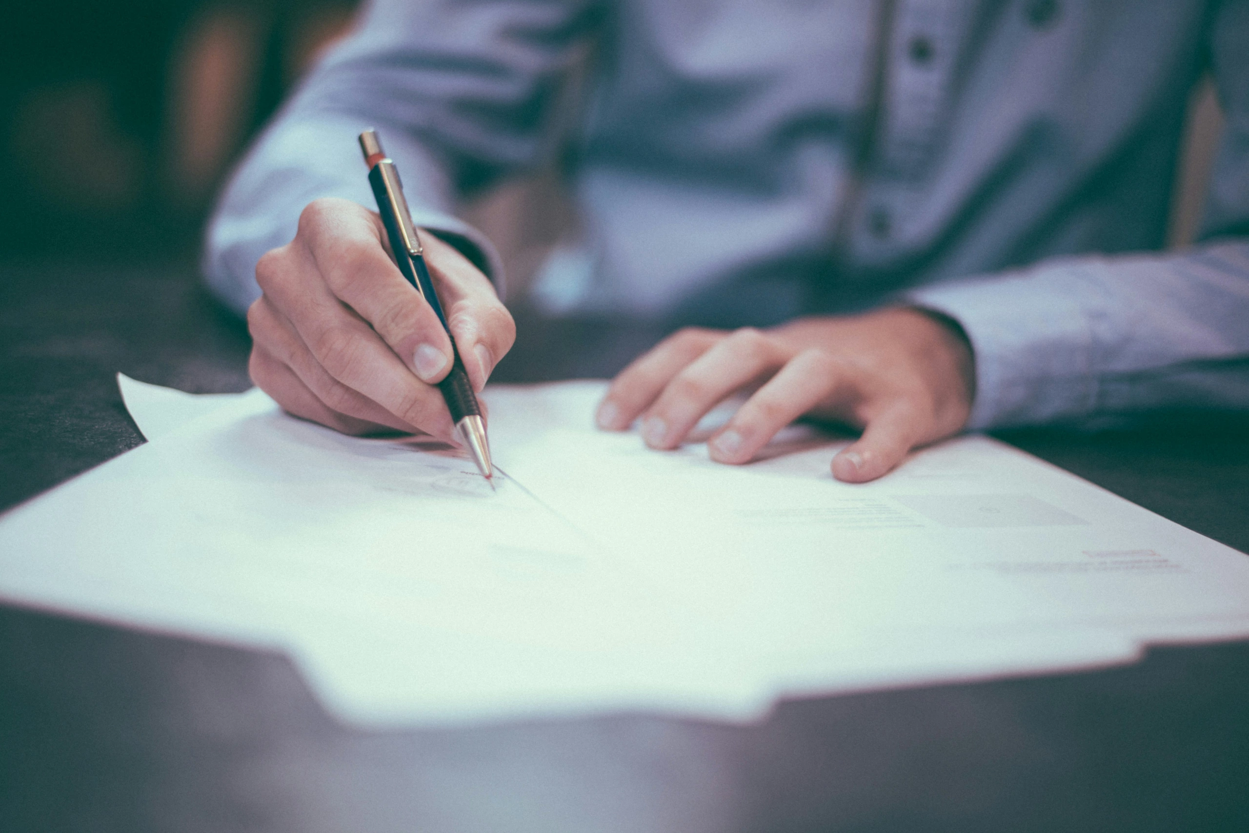 Une personne vêtue d'une chemise à manches longues est assise à un bureau et remplit à l'aide d'un stylo les formulaires de certificat d'authenticité pour les tirages de studio.