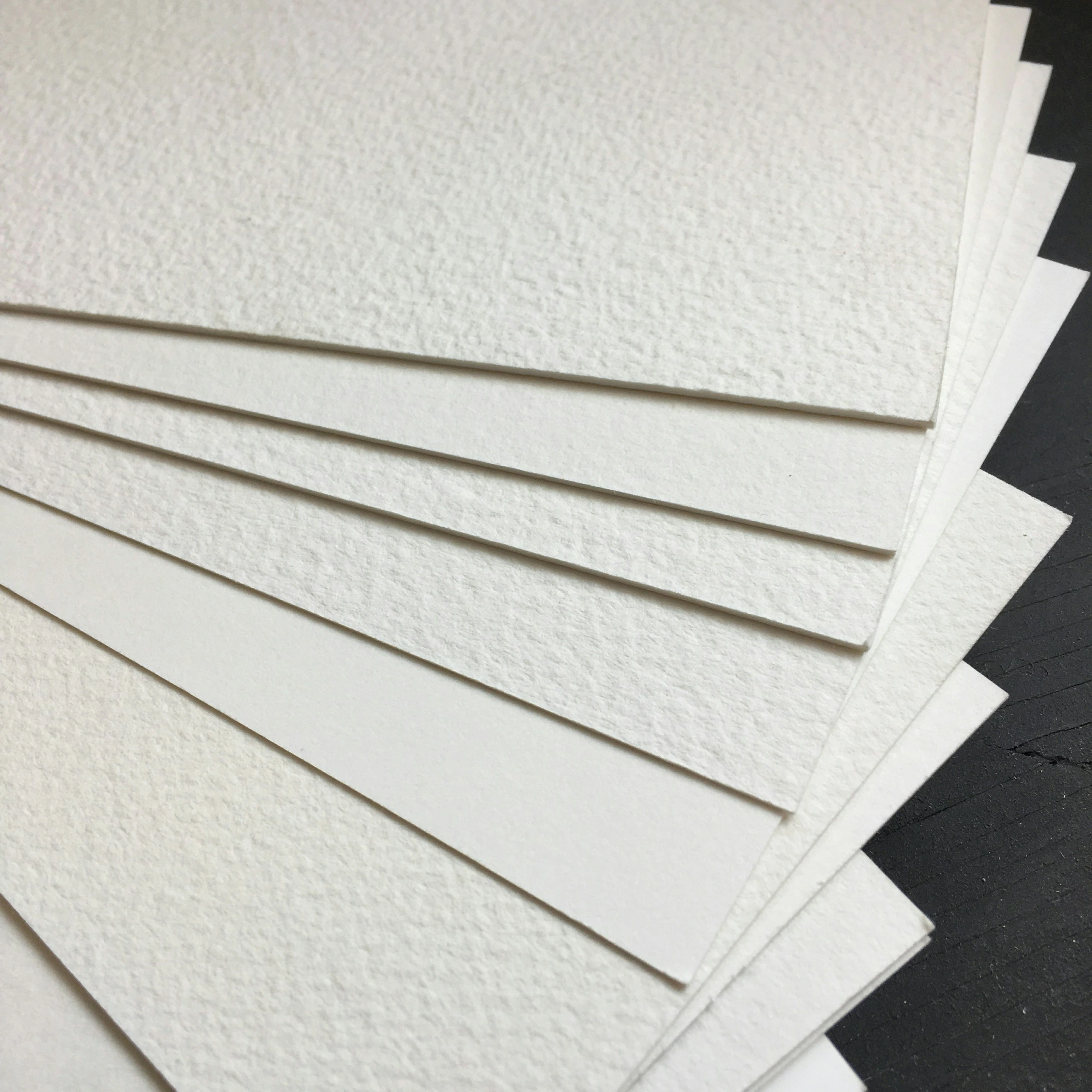 Macro prise de vue de feuilles de papier d'art blanc, disposées en éventail sur un fond sombre, mettant en évidence la surface texturée idéale pour l'impression de photos.