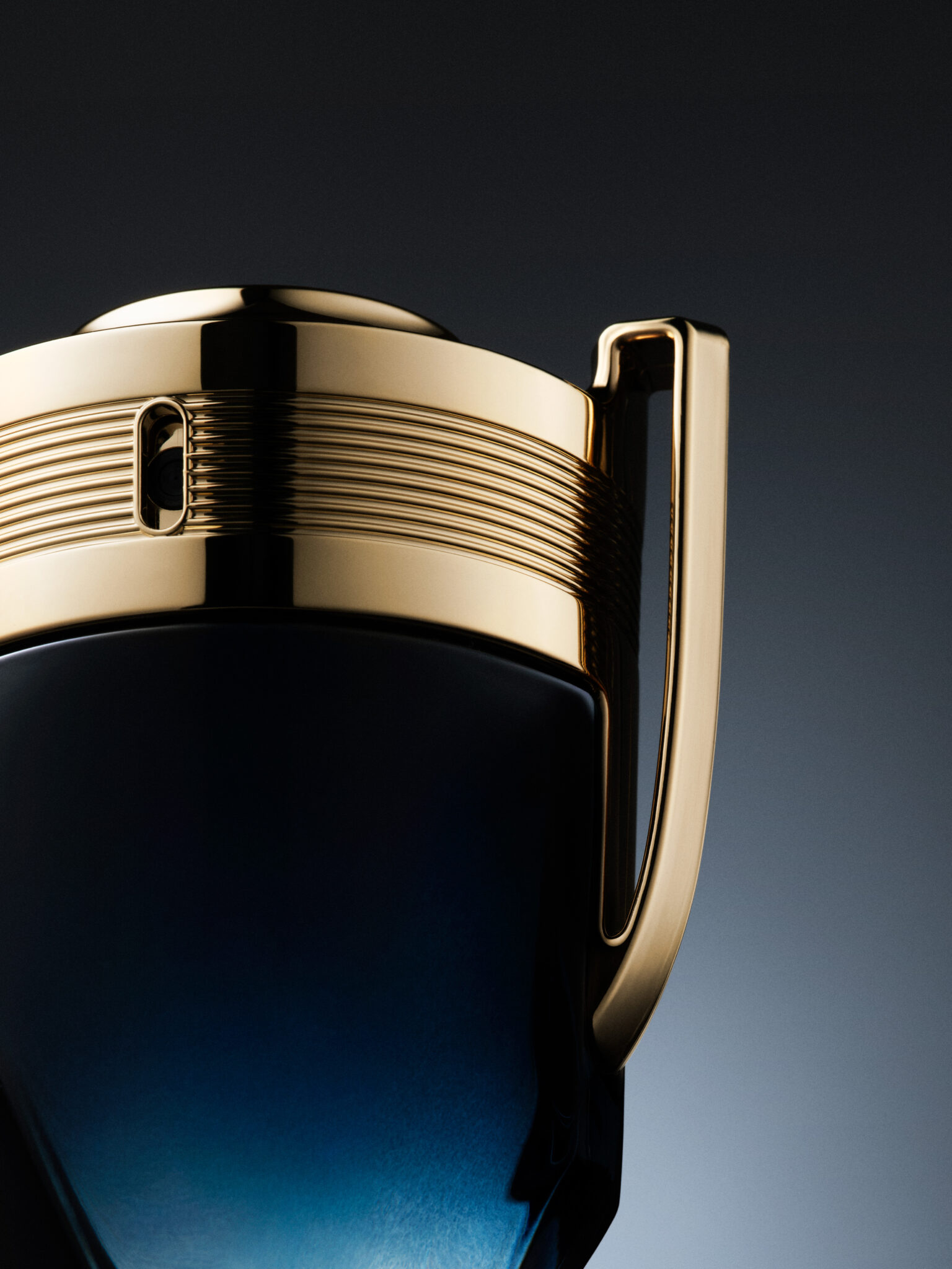 INVICTUS_PARFUM Gros plan en studio d'un objet en forme de trophée avec une poignée et un bord dorés, un corps bleu-noir, sur un fond sombre dégradé.