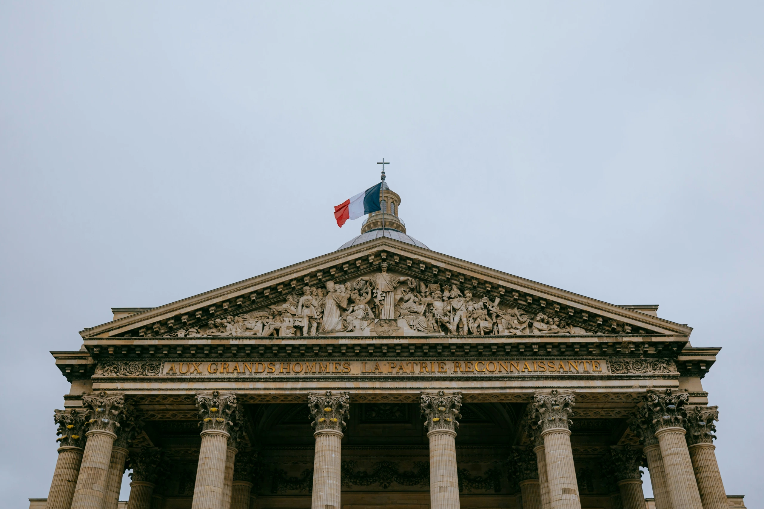 Façade de bâtiment néoclassique avec colonnes et fronton détaillé, petite coupole, drapeau français, photographiée sous un éclairage doux et diffus.