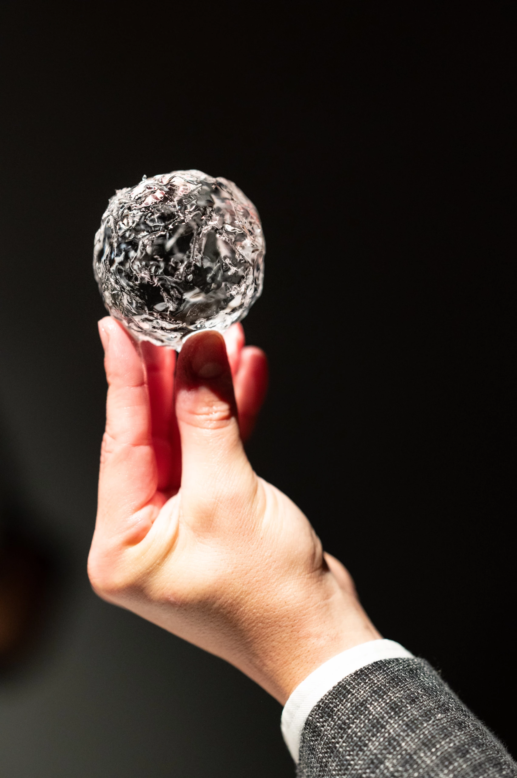 Une main tient une sphère de glace parfaitement taillée sur fond noir.