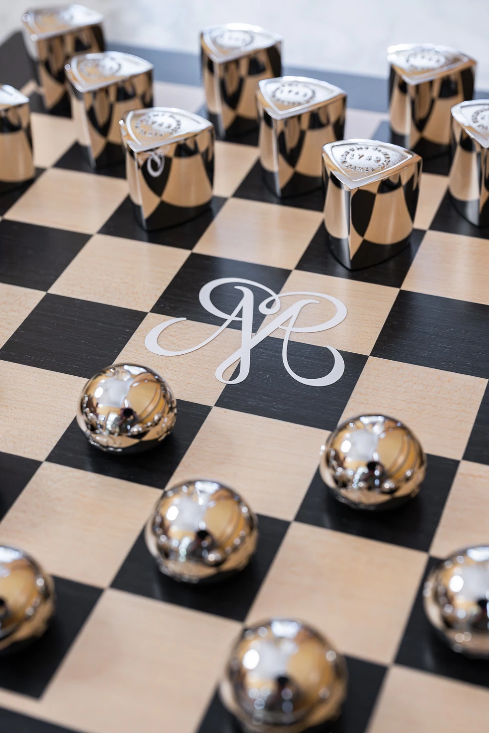 Jeu d’échecs personnalisé Parfums de Marly, composé de pièces métalliques argentées sur un plateau gravé du monogramme de la marque.