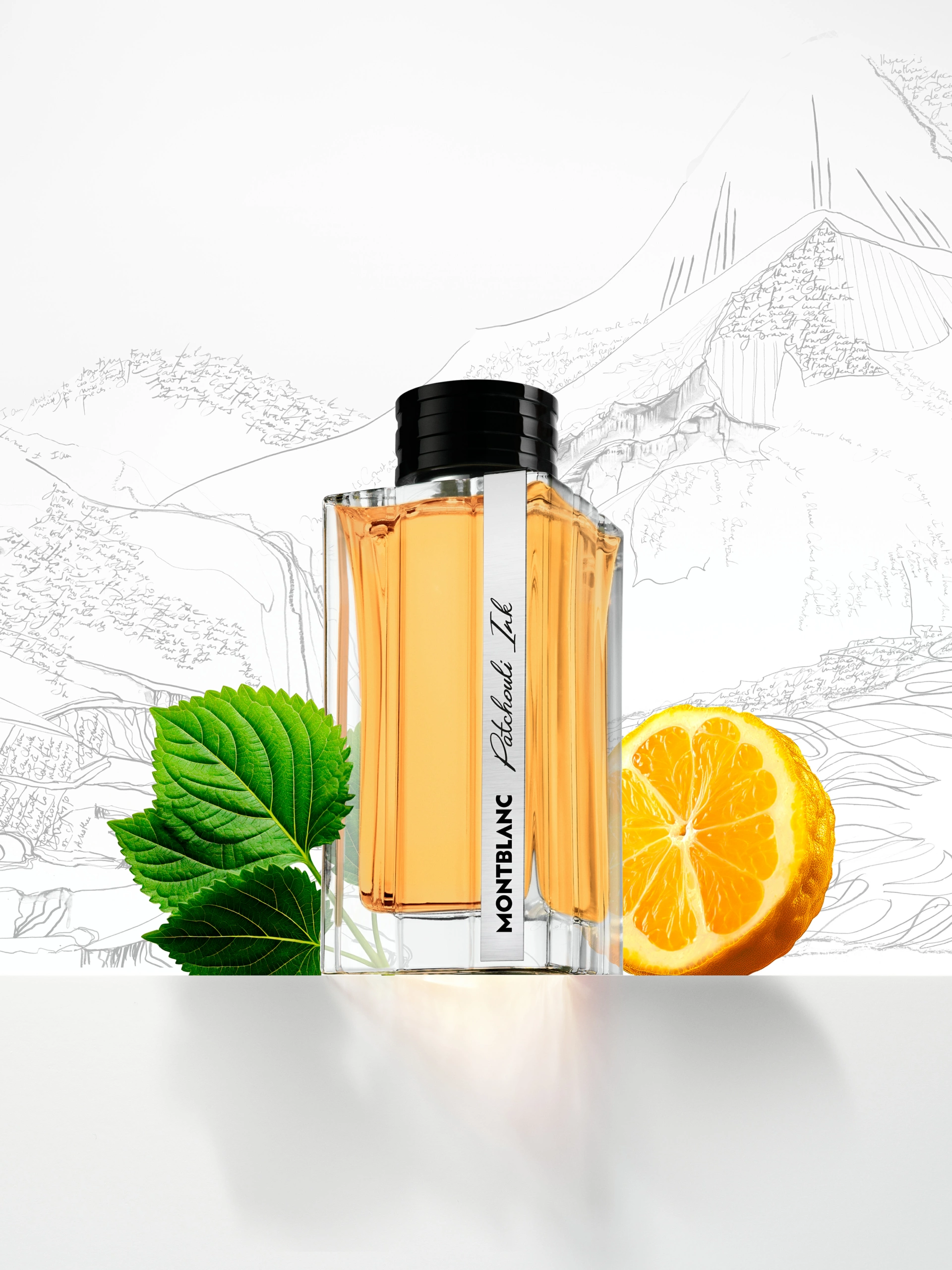 SOLO_MONTBLANC_PATCHOULI_INK_R3 Un flacon de parfum Montblanc contenant un liquide de couleur ambrée, posé sur un décor de studio avec une montagne esquissée en arrière-plan, accompagné d'une feuille verte et d'une orange coupée en deux pour une séance photo de produit.